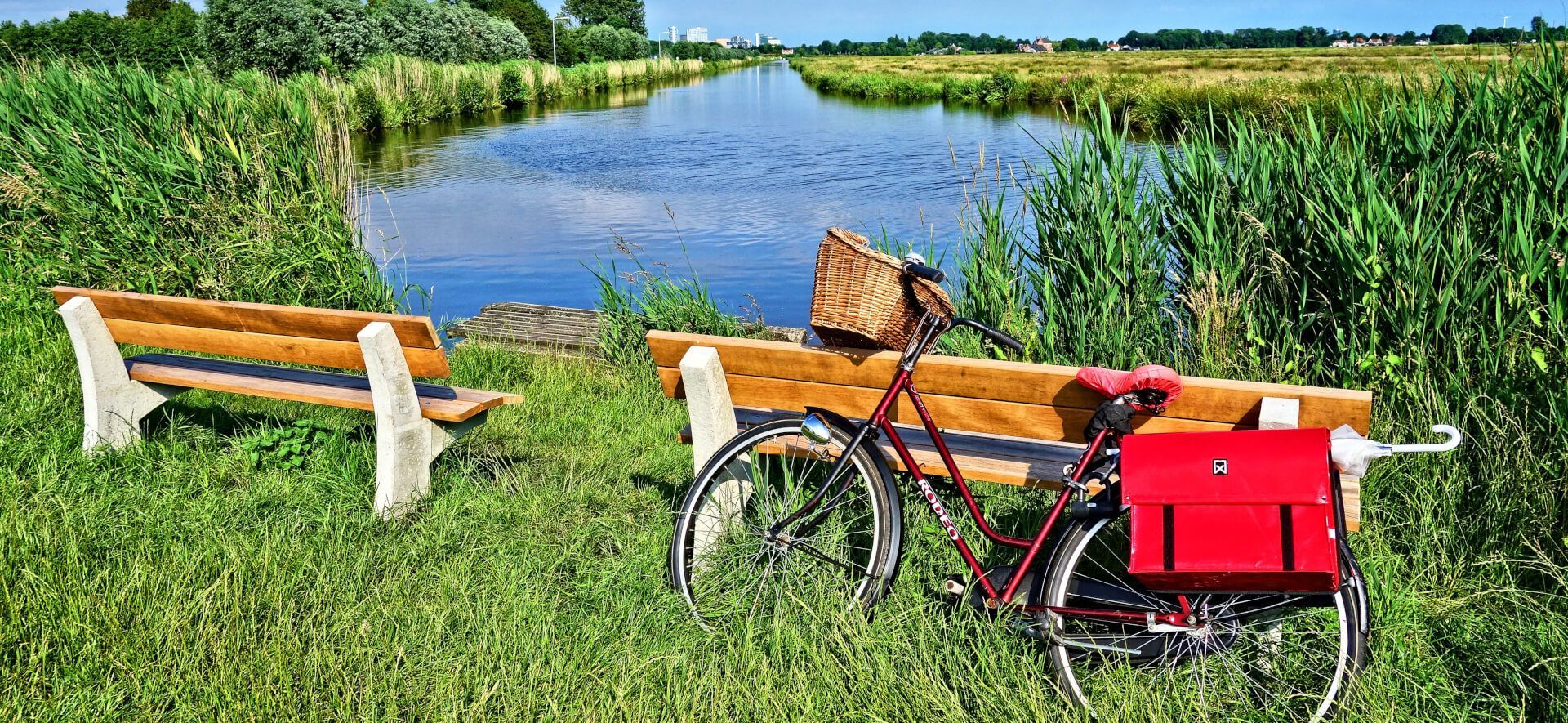 Een fiets staat geparkeerd naast een houten bankje naast een rivier.