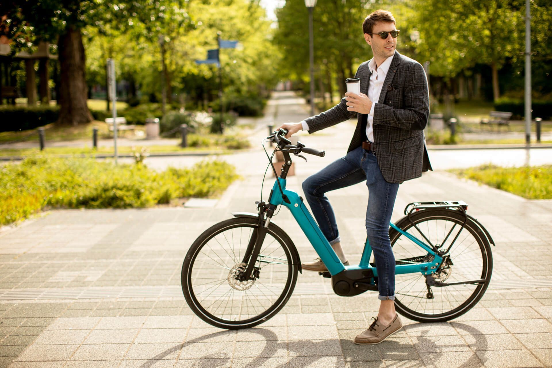 Een man in pak rijdt op een elektrische fiets op de stoep.