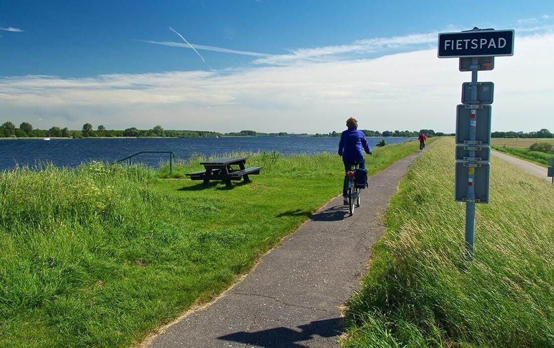 Een persoon fietst op een pad naast een meer.