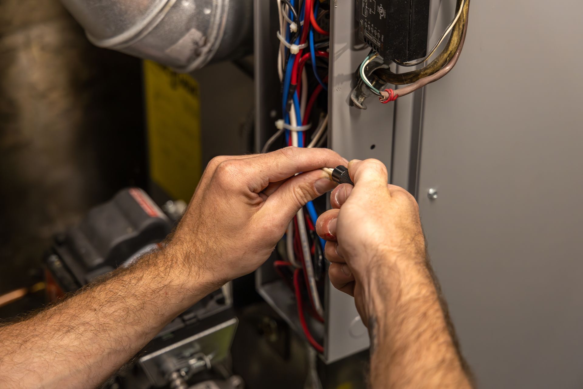 Technician in orange hard hat using a multimeter to test wiring in an electrical panel
