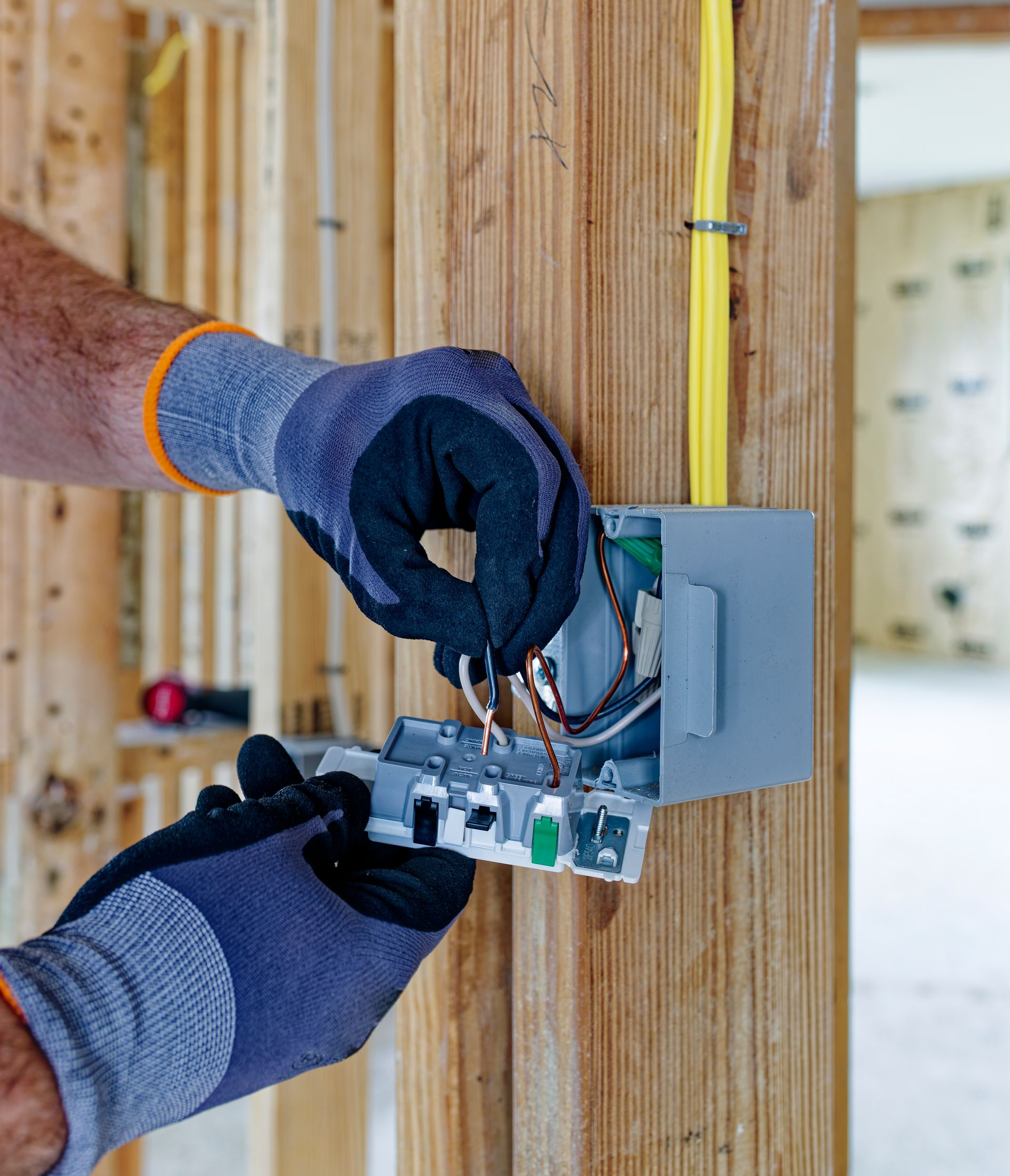 Hands using orange-handled pliers to strip a wire in an electrical panel
