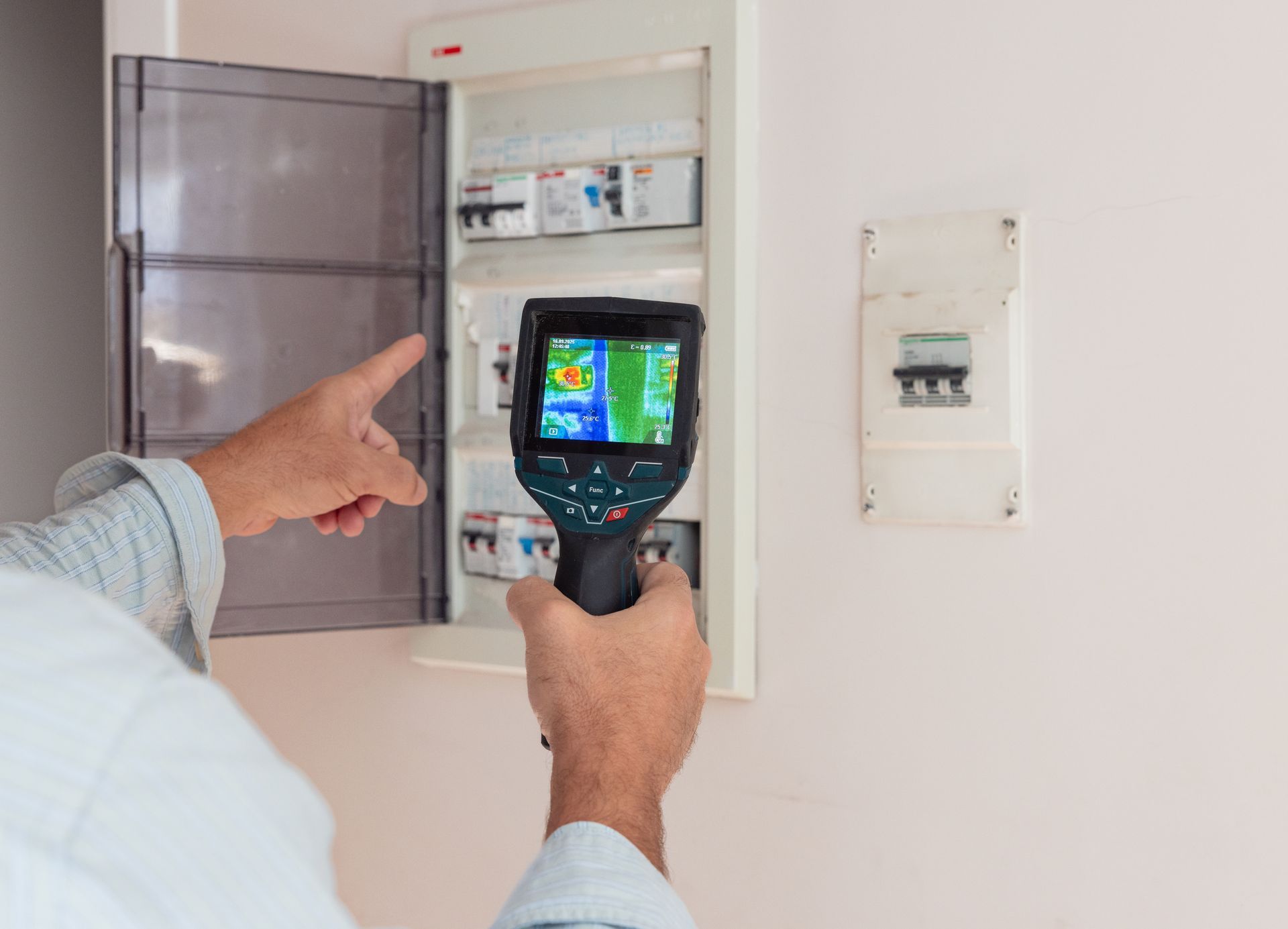 Person using a thermal camera to inspect an electrical panel on a wall