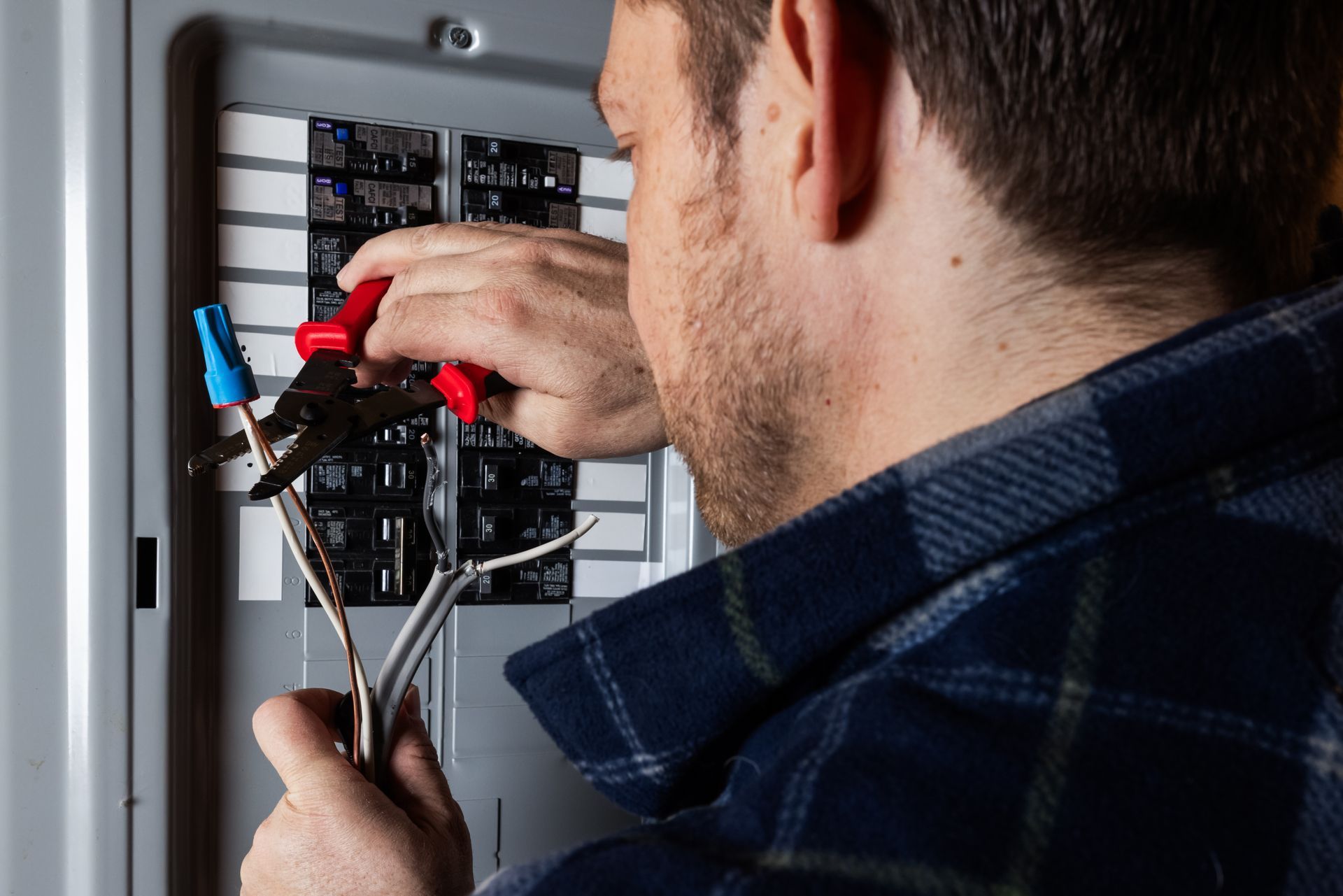 Technician testing an electrical panel with a multimeter, wearing a yellow hard hat