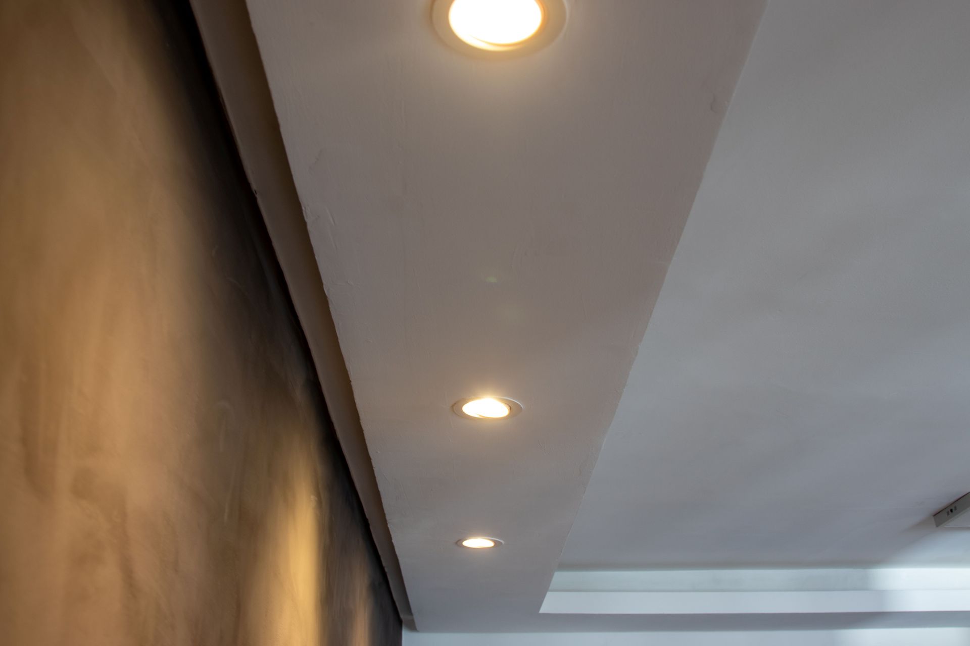 Recessed ceiling lights along a white ceiling beside a dark textured wall