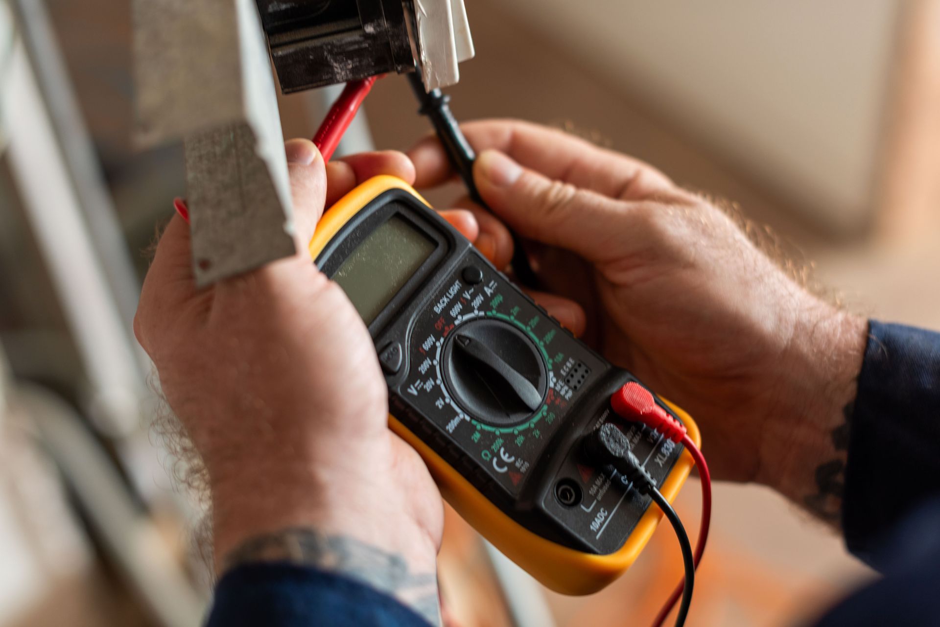 Person using a digital multimeter to test electrical wiring indoors