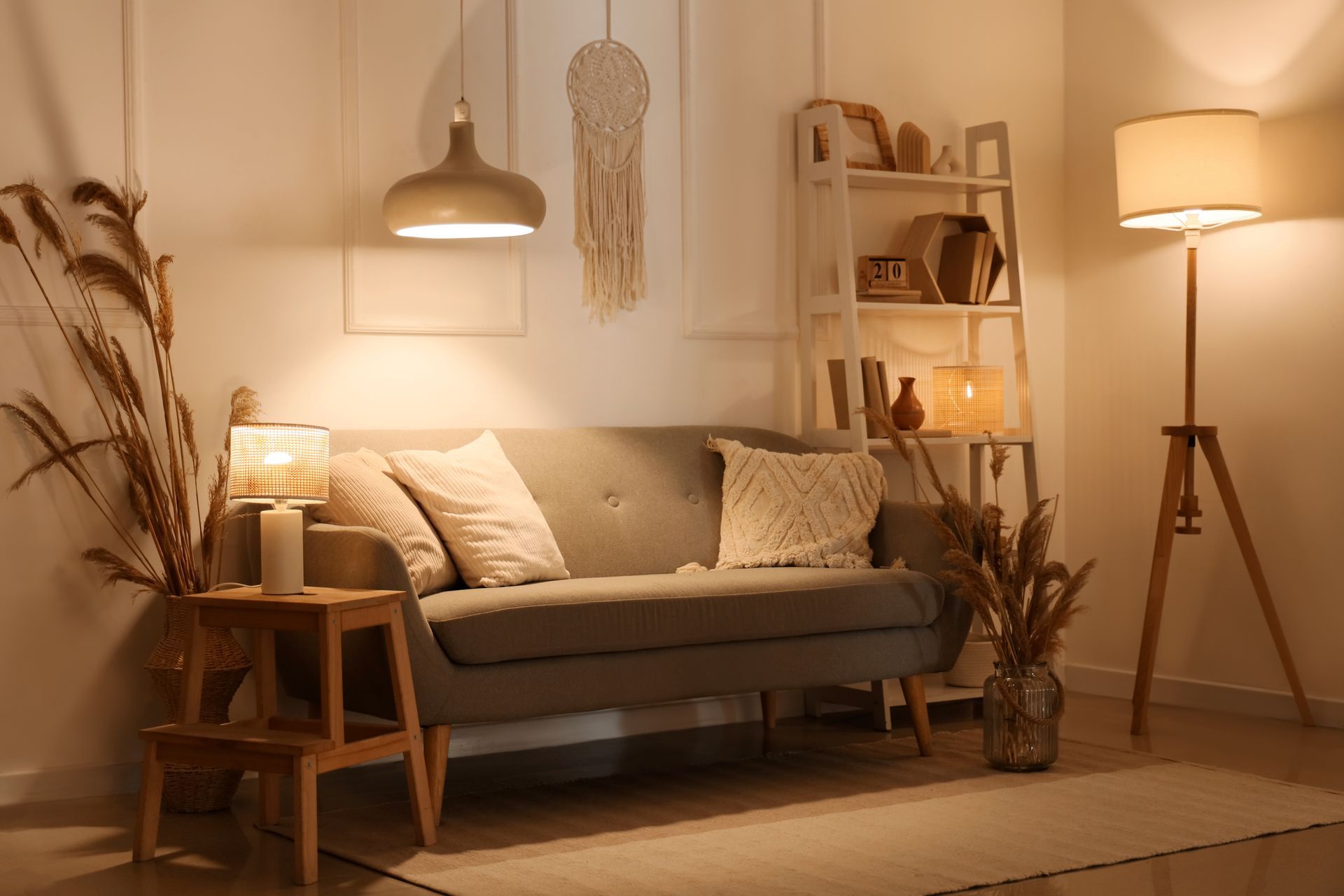 Cozy beige living room with sofa, floor lamp, side table, and dried plants in warm lighting