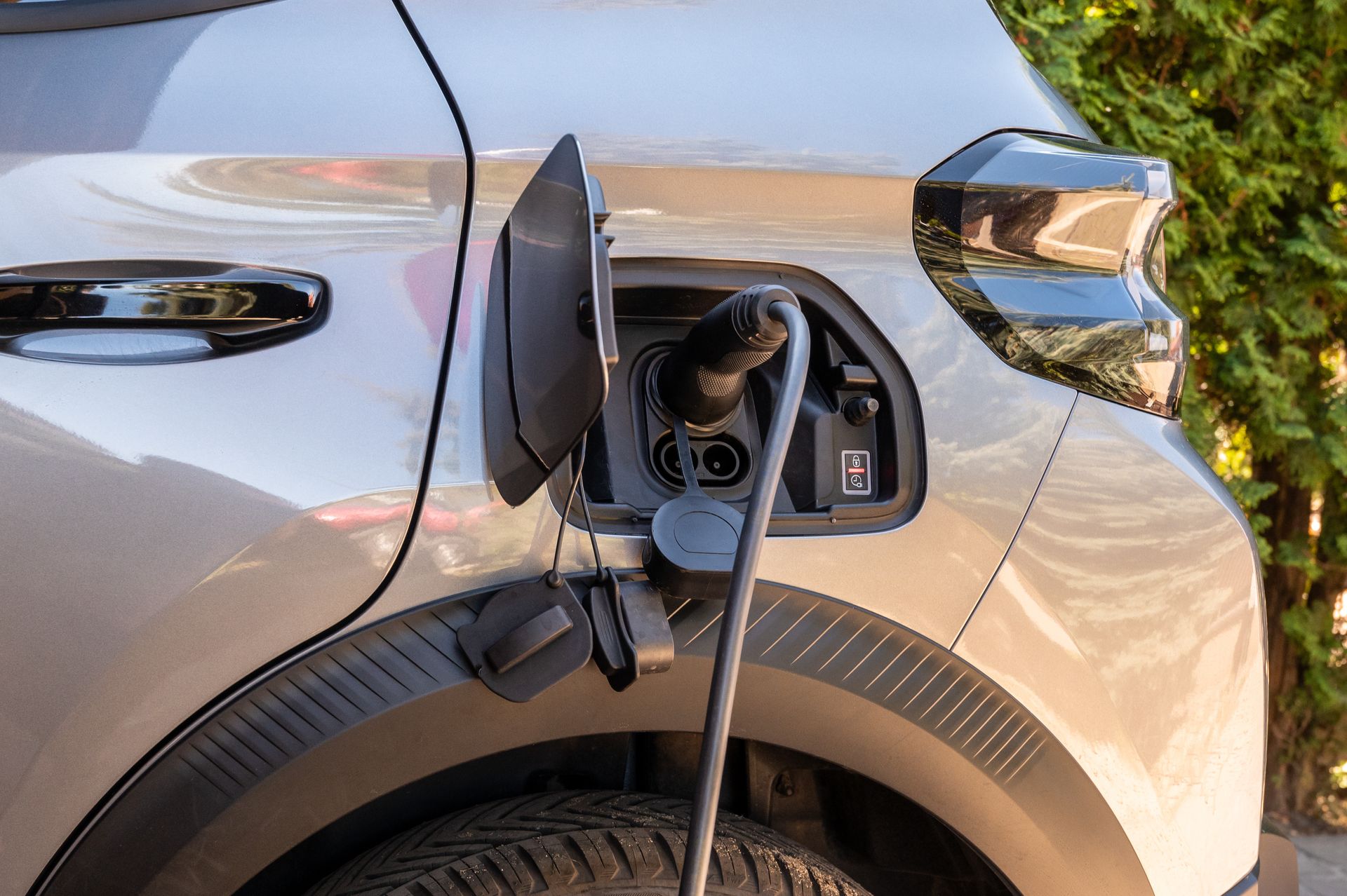 Electric car charging at a roadside station, with a cable plugged into the front fender port.