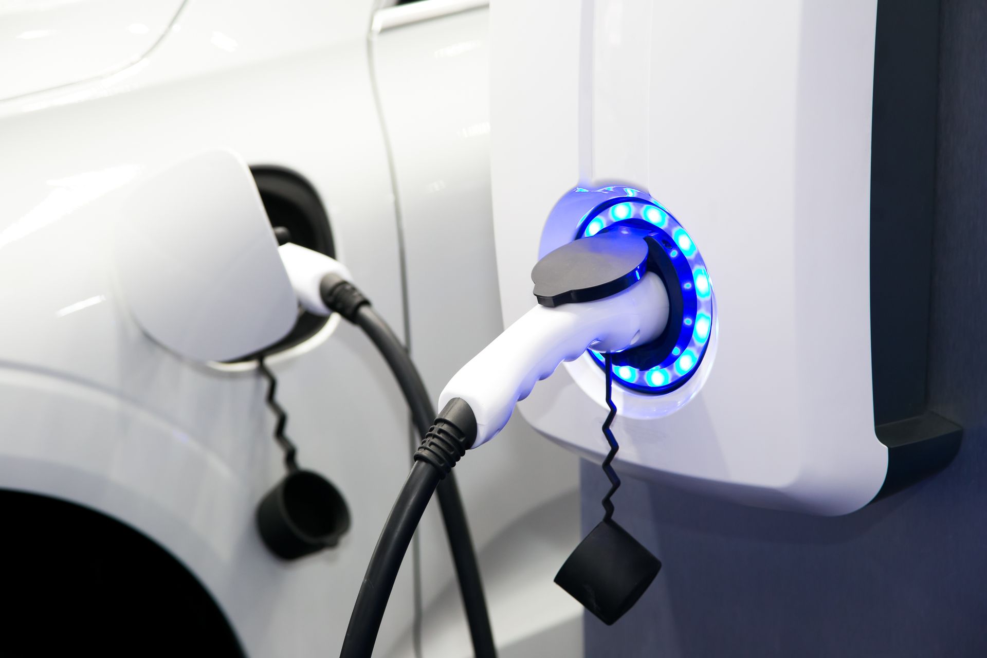 Electric car charging at a wall-mounted station with a blue illuminated ring