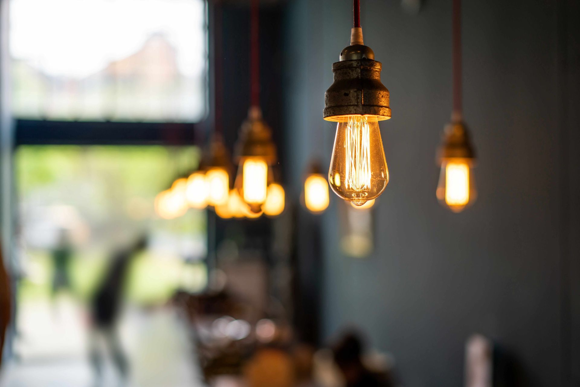 Warm hanging Edison bulbs in a blurred café interior with a window in the background