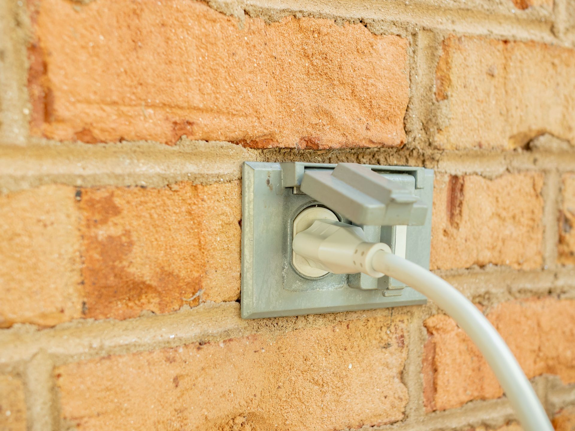 White cable plugged into a wall outlet on a brick wall.