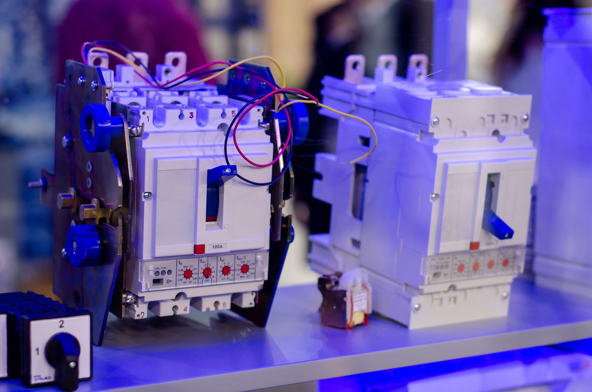 Two industrial electrical contactors on a blue-lit display table, with wires attached to the left unit