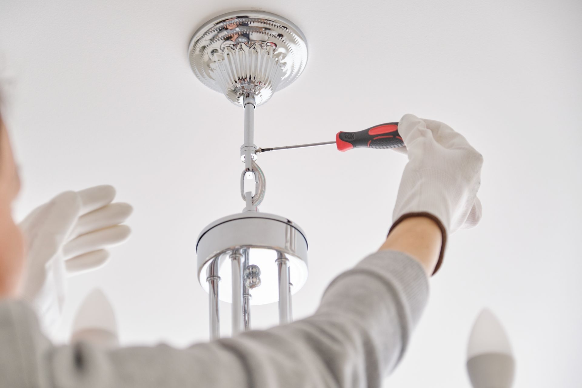 Person tightening a chandelier hook with a screwdriver while wearing white gloves