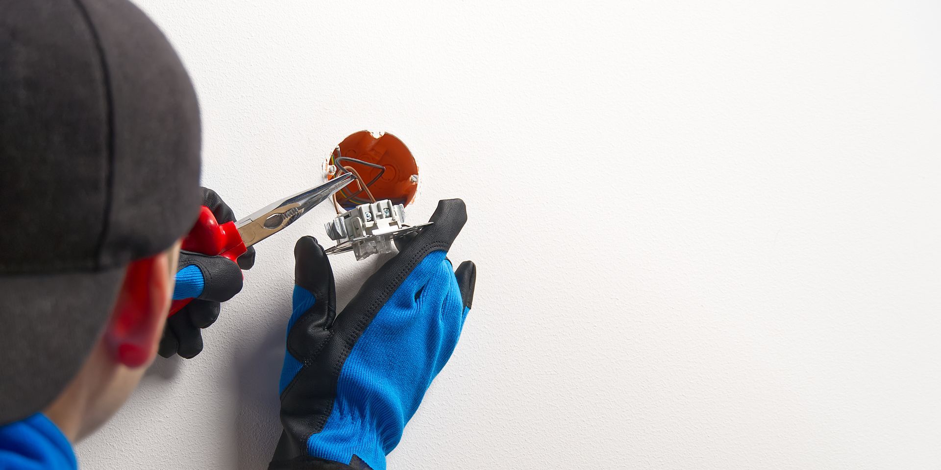 Person in blue gloves using a hand tool to work on an orange circular object against a white background