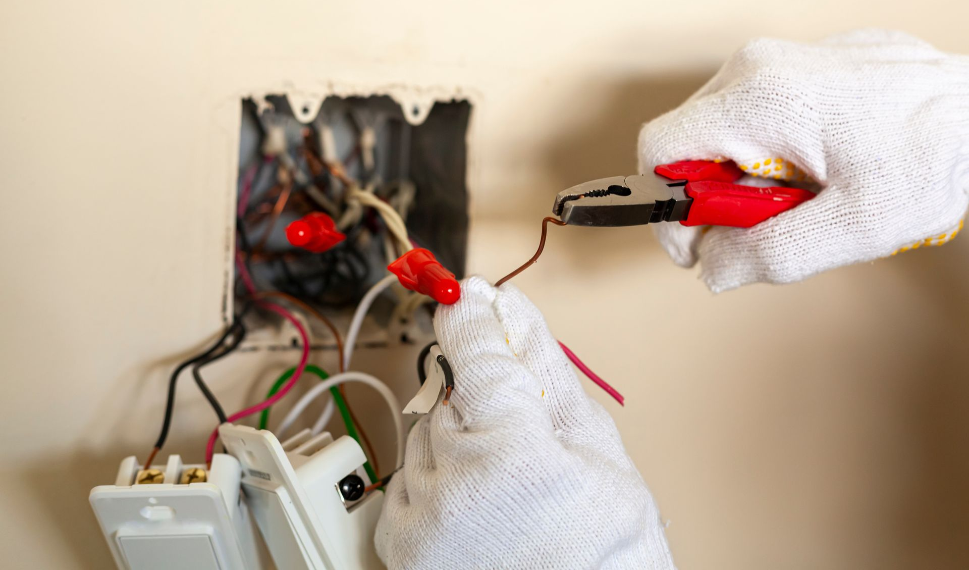 Gloved hands testing wires with a multimeter near an electrical panel and tools