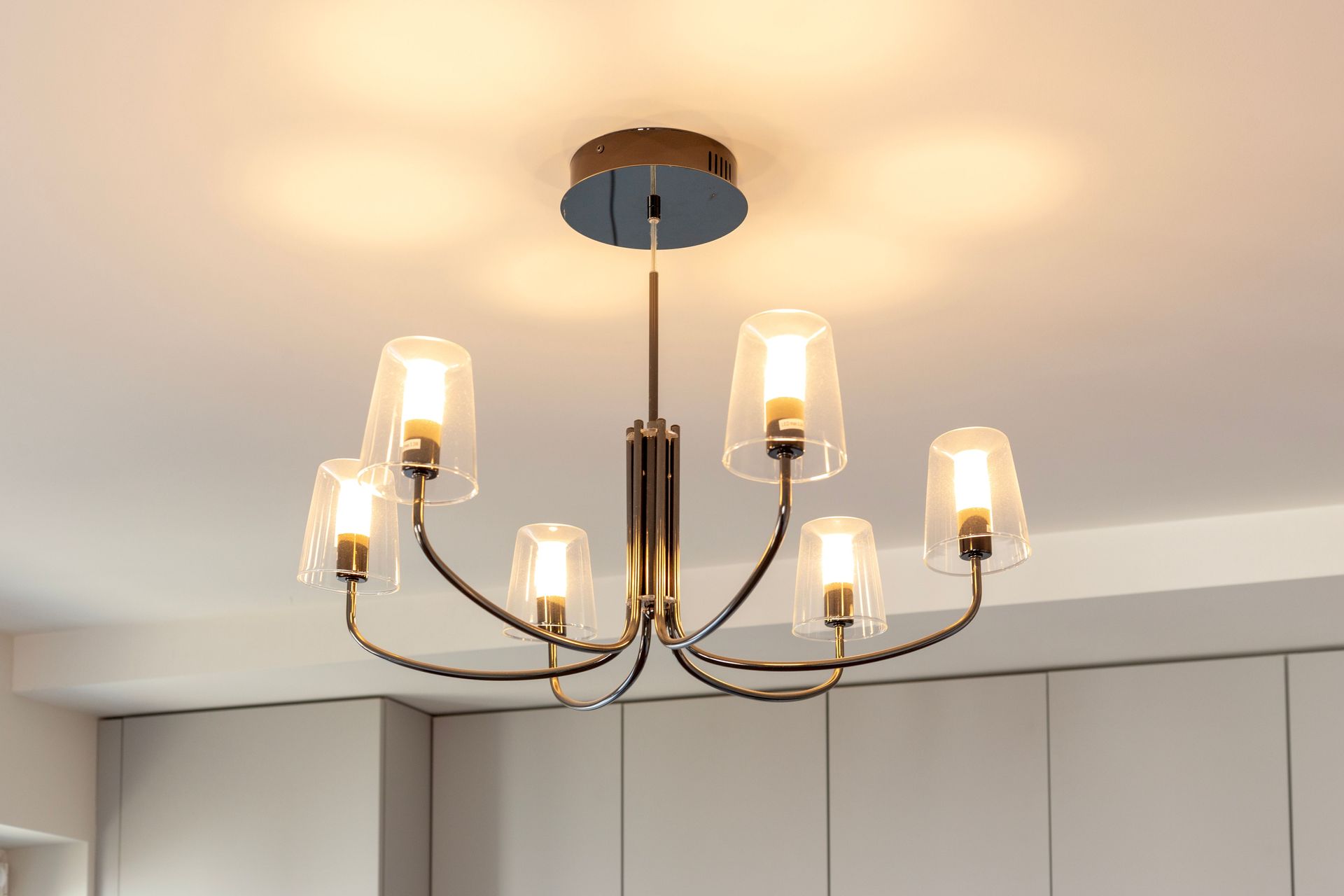 Modern chandelier with six glass shades on a ceiling in a bright room
