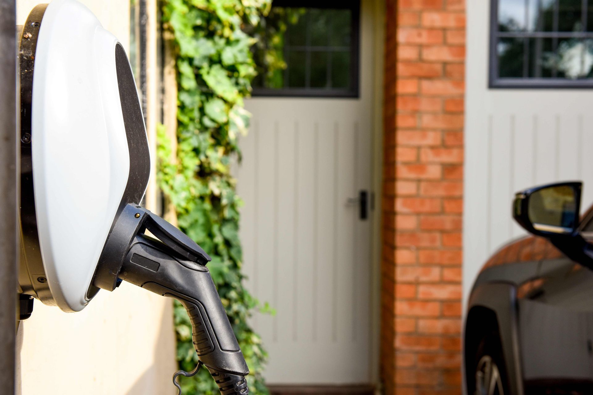 Electric vehicle charging plug connected to a wall charger beside a car in a driveway