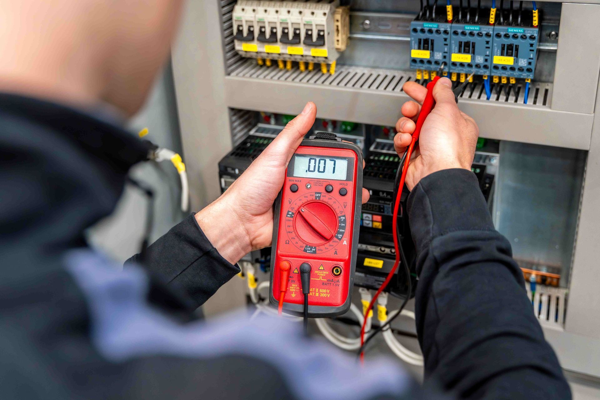 Technician testing electrical panel with red multimeter and probes