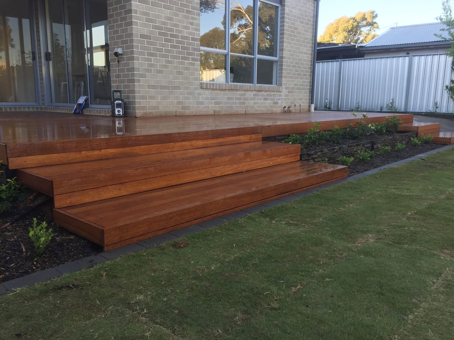 Wooden front porch steps beside a brick house and lawn, with garden beds along the walkway.