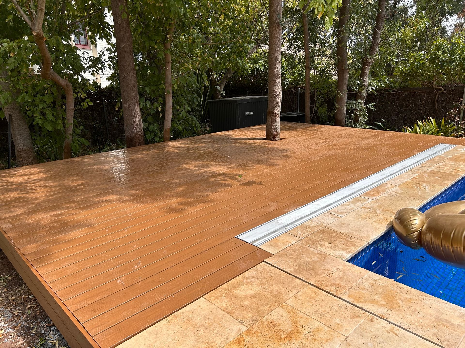 Wooden pool deck beside a blue swimming pool with a stone sculpture and trees nearby
