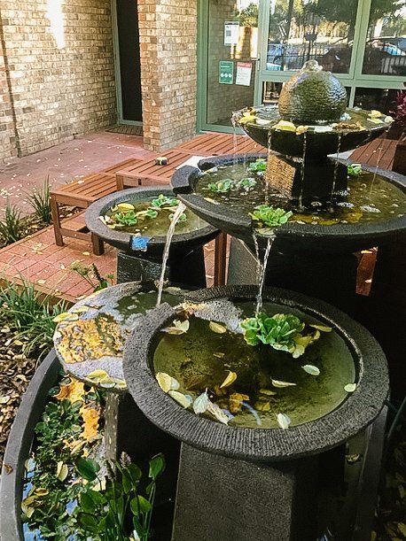 Three black outdoor fountains with water lilies beside a brick patio and wall