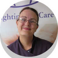 Woman wearing glasses smiles in front of a logo with blue text on a white background.