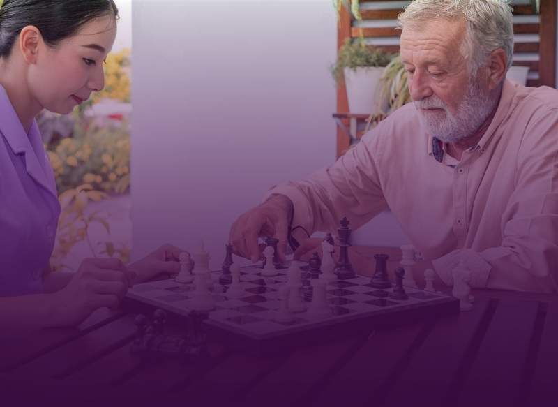 Woman and man playing chess outdoors, man moving a piece.