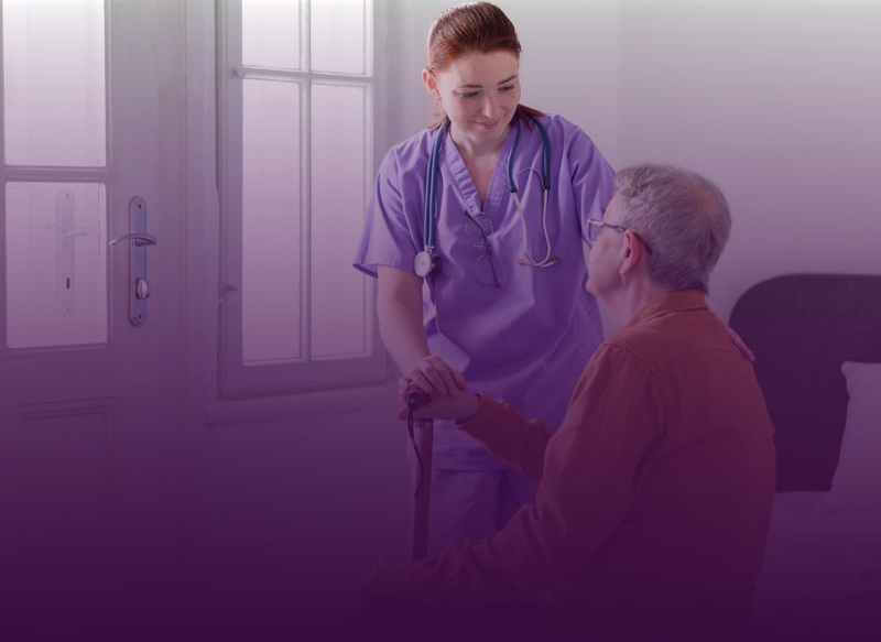 Nurse in purple scrubs assisting a person with a cane indoors, near a window.