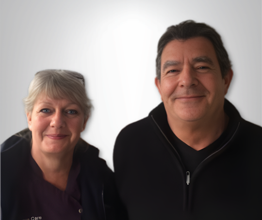 Woman and man smiling, both facing the camera. Neutral background, man wearing black jacket, woman wearing dark top.