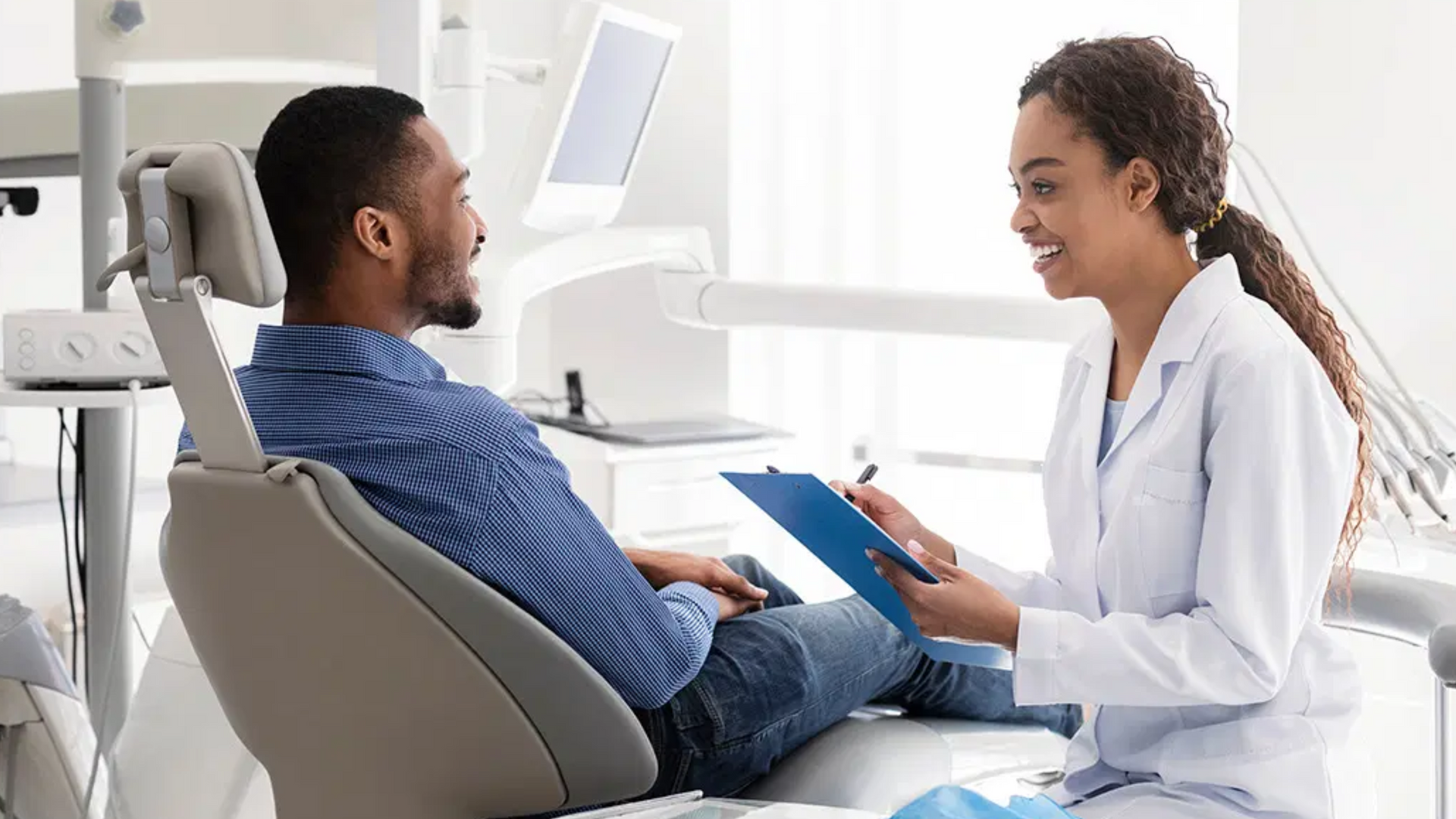 Patient discussing treatment with dentist in a bright dental clinic, holding a blue folder