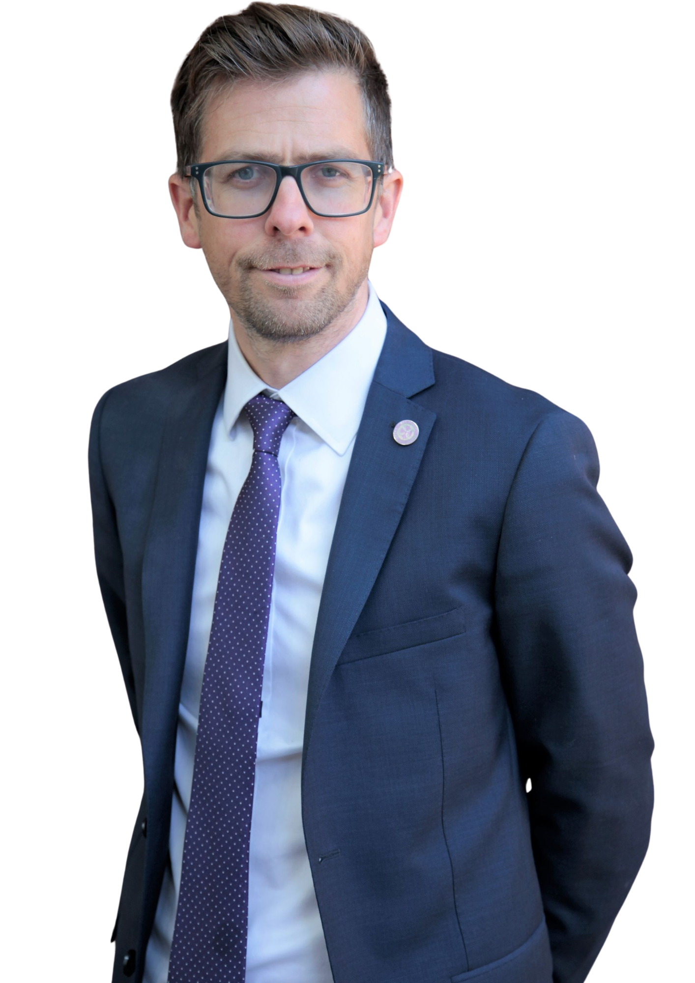 Man in a suit and tie with glasses, standing against a plain background.