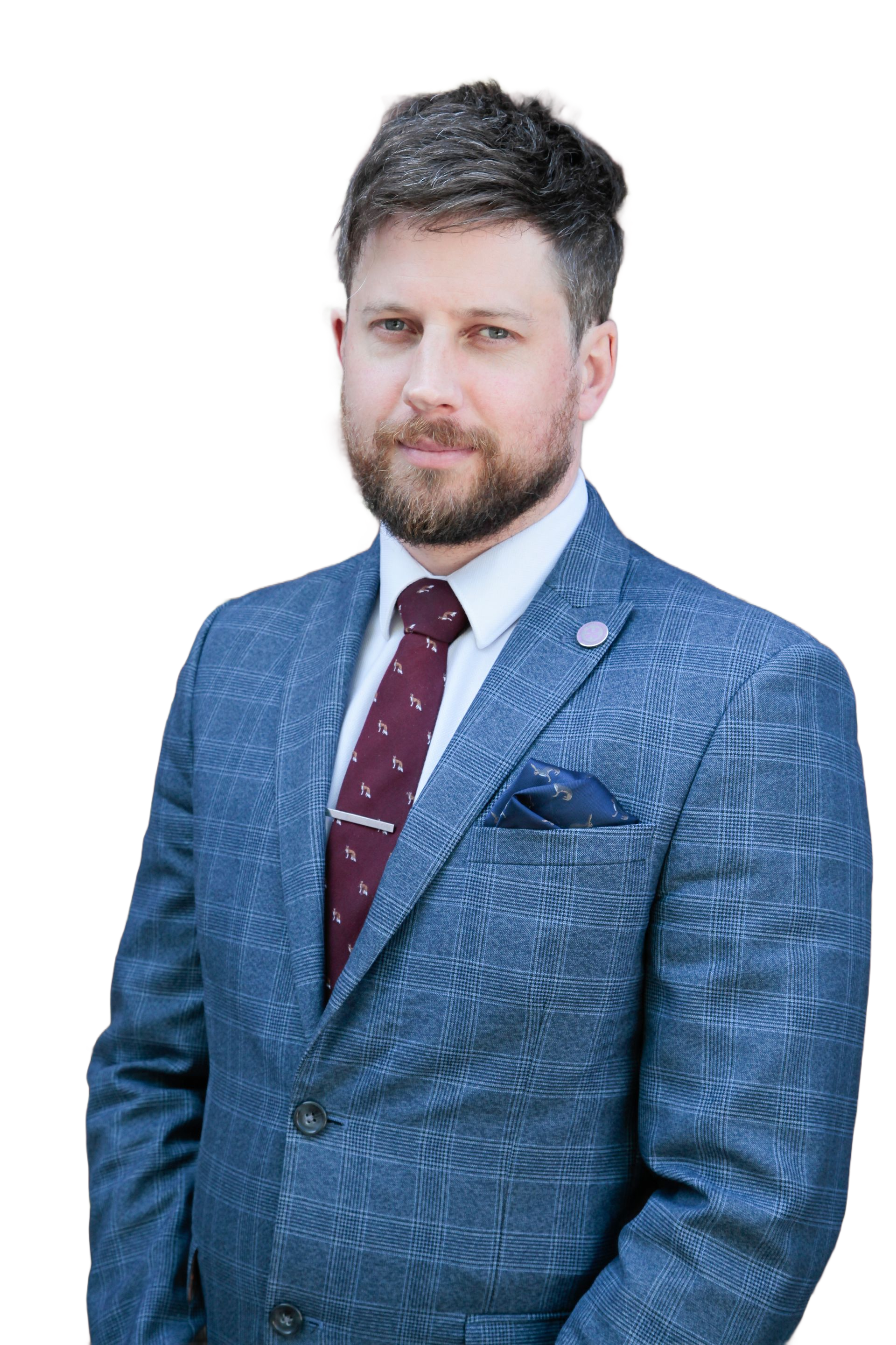 Smiling bearded man in a suit and tie with a pocket square, standing against a bright background