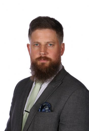 Portrait of a bearded man in a gray suit with a light green tie and blue pocket square on a white background