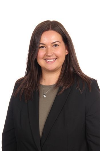 Smiling woman in a black blazer over an olive top against a white background