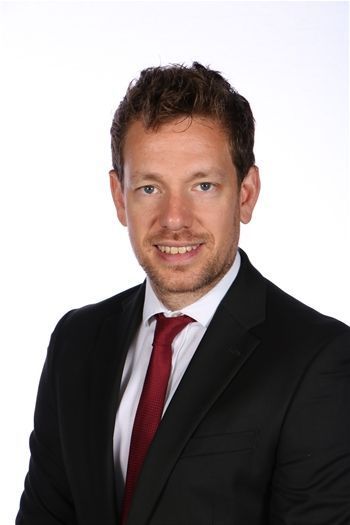 Portrait of a man in a black suit, white shirt, and red tie against a white background.