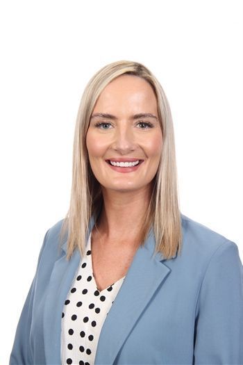 Smiling professional in a blazer, posed against a plain light background.