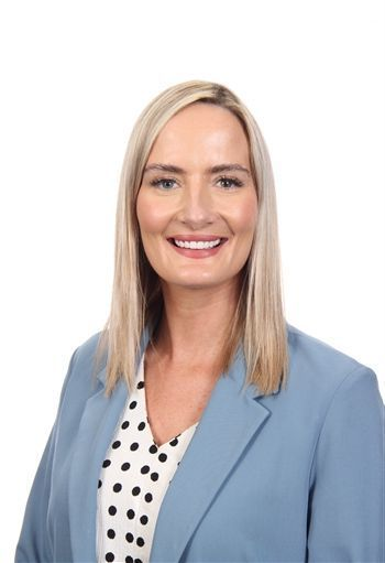 Portrait of a smiling woman in a light blue blazer and polka dot blouse against a white background