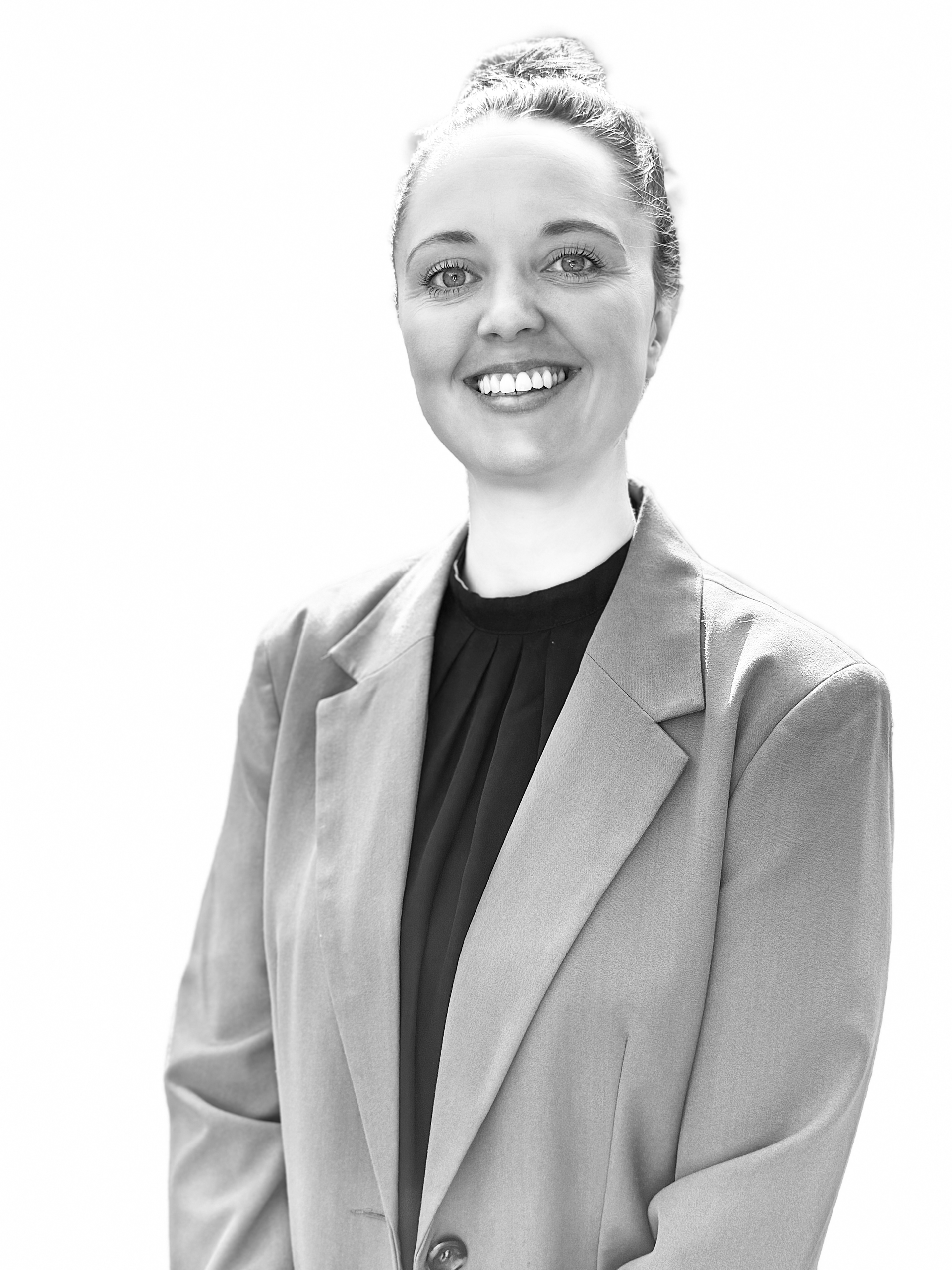 Smiling person in a light blazer over a dark top, standing against a plain background.
