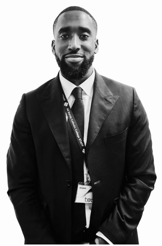 Man in a dark suit and tie standing against a plain background, wearing a lanyard and smiling.