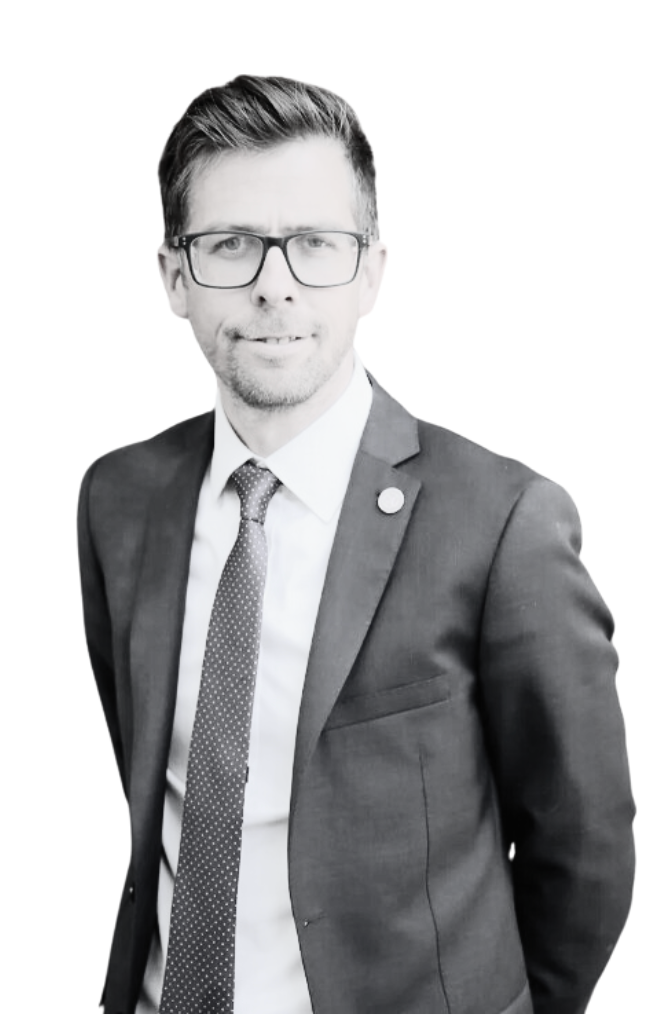 Man in a suit and tie with glasses, standing against a plain background.