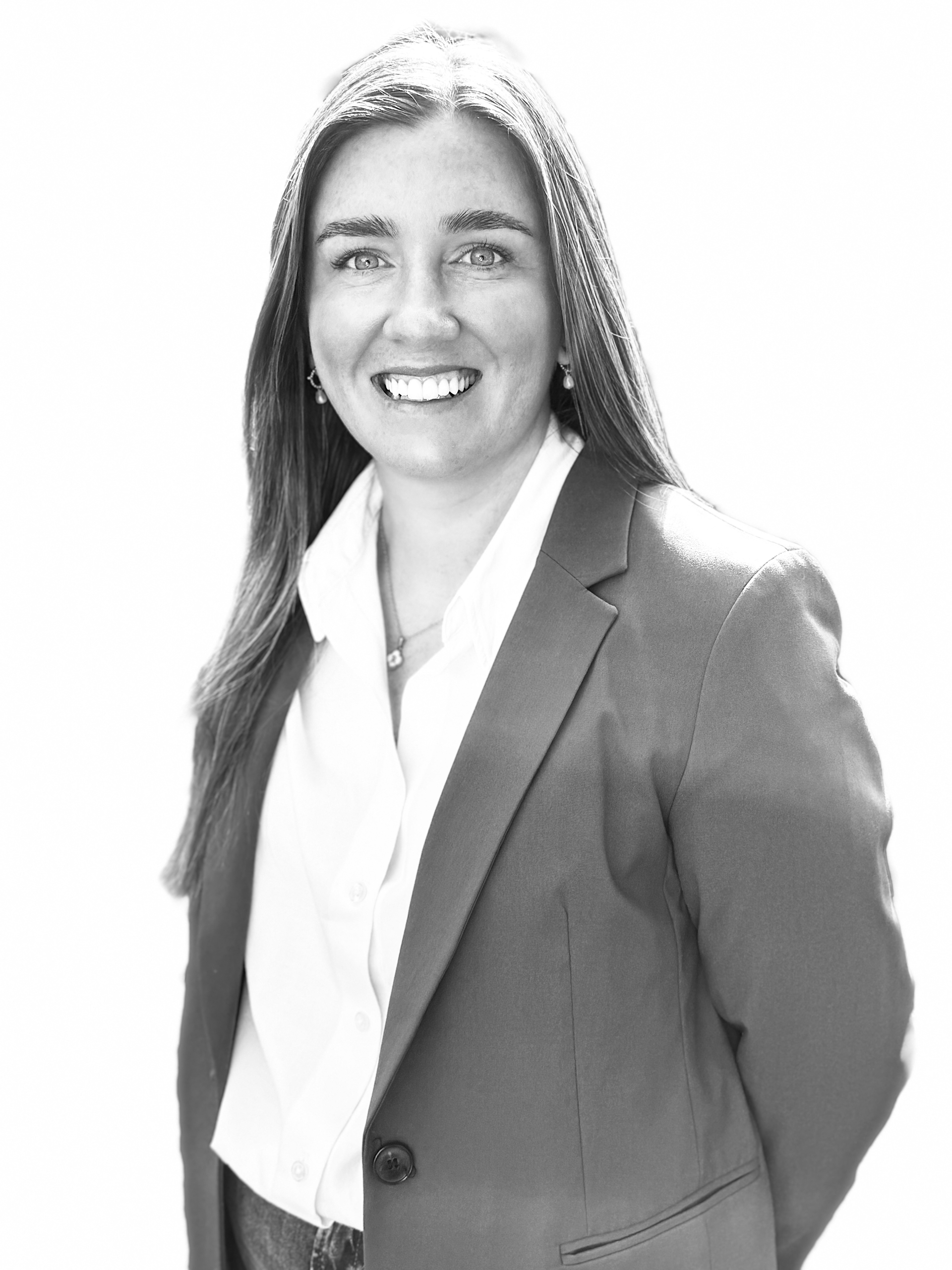 Smiling person in a blazer and white blouse, standing against a bright background