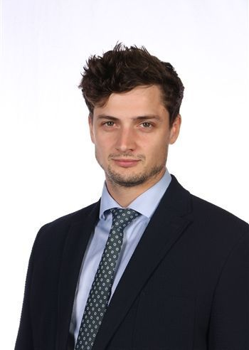 Studio portrait of a man in a dark suit and patterned tie against a white background