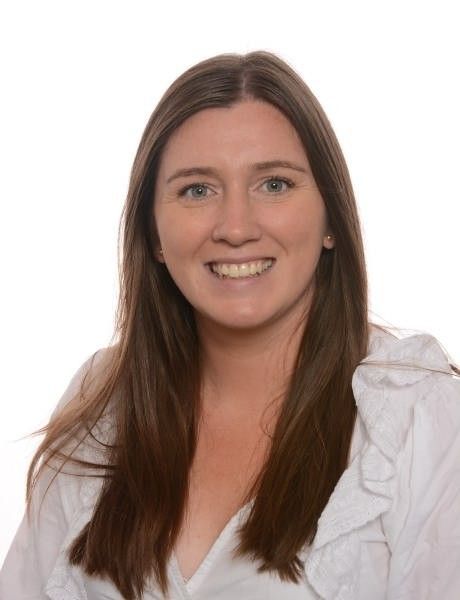 Smiling person in a blazer and white blouse, standing against a bright background