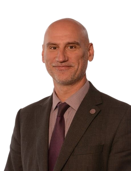 Man in a suit and tie standing against a white background, smiling slightly.