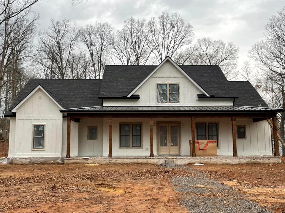 A white house with a black roof is sitting on top of a dirt field.