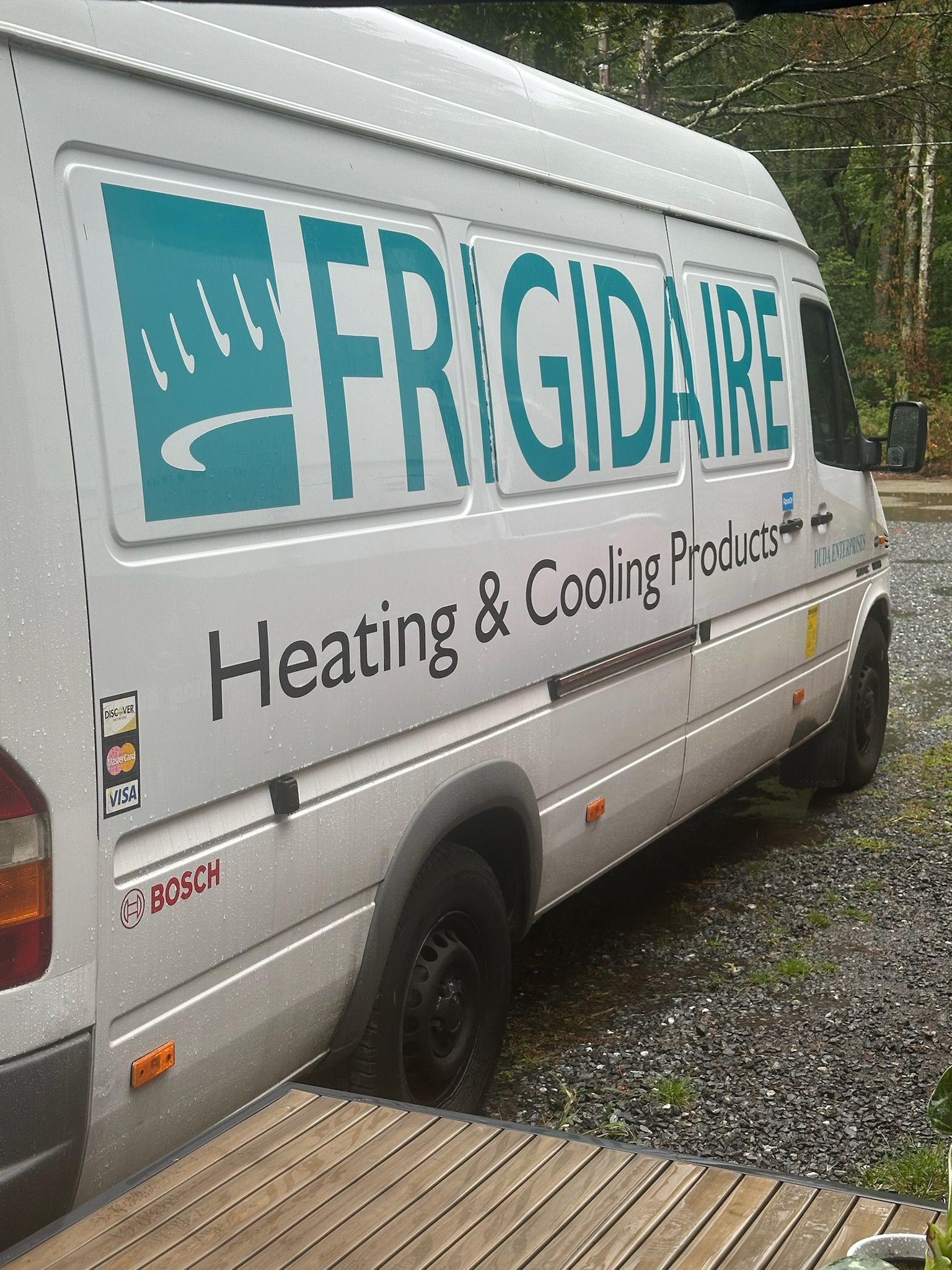 White Frigidaire service van parked on a gravel driveway, with teal logo and