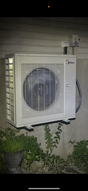 Outdoor wall-mounted air conditioner unit beside a house at night