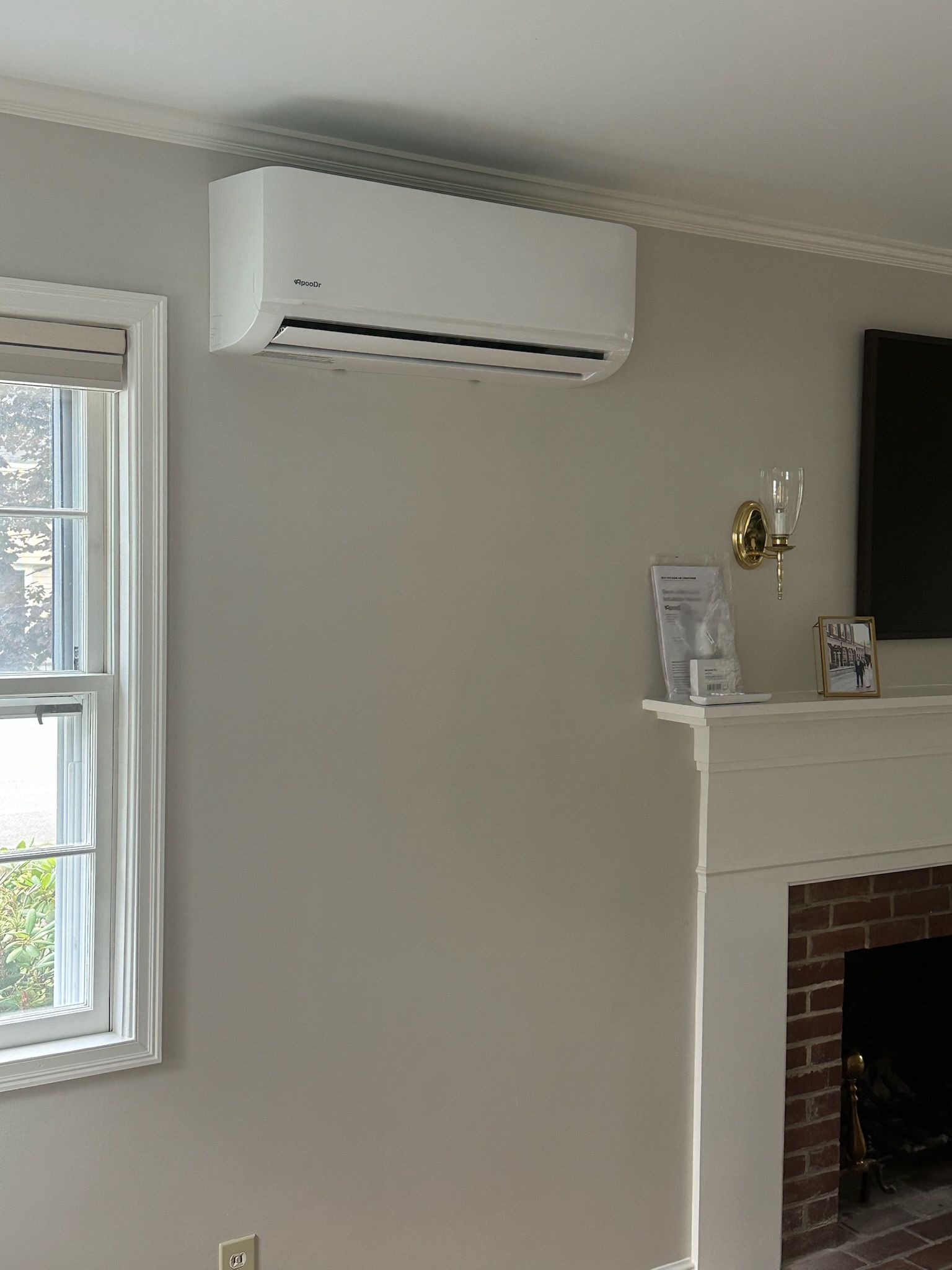 Living room wall with a white air conditioner above a fireplace and window on the left