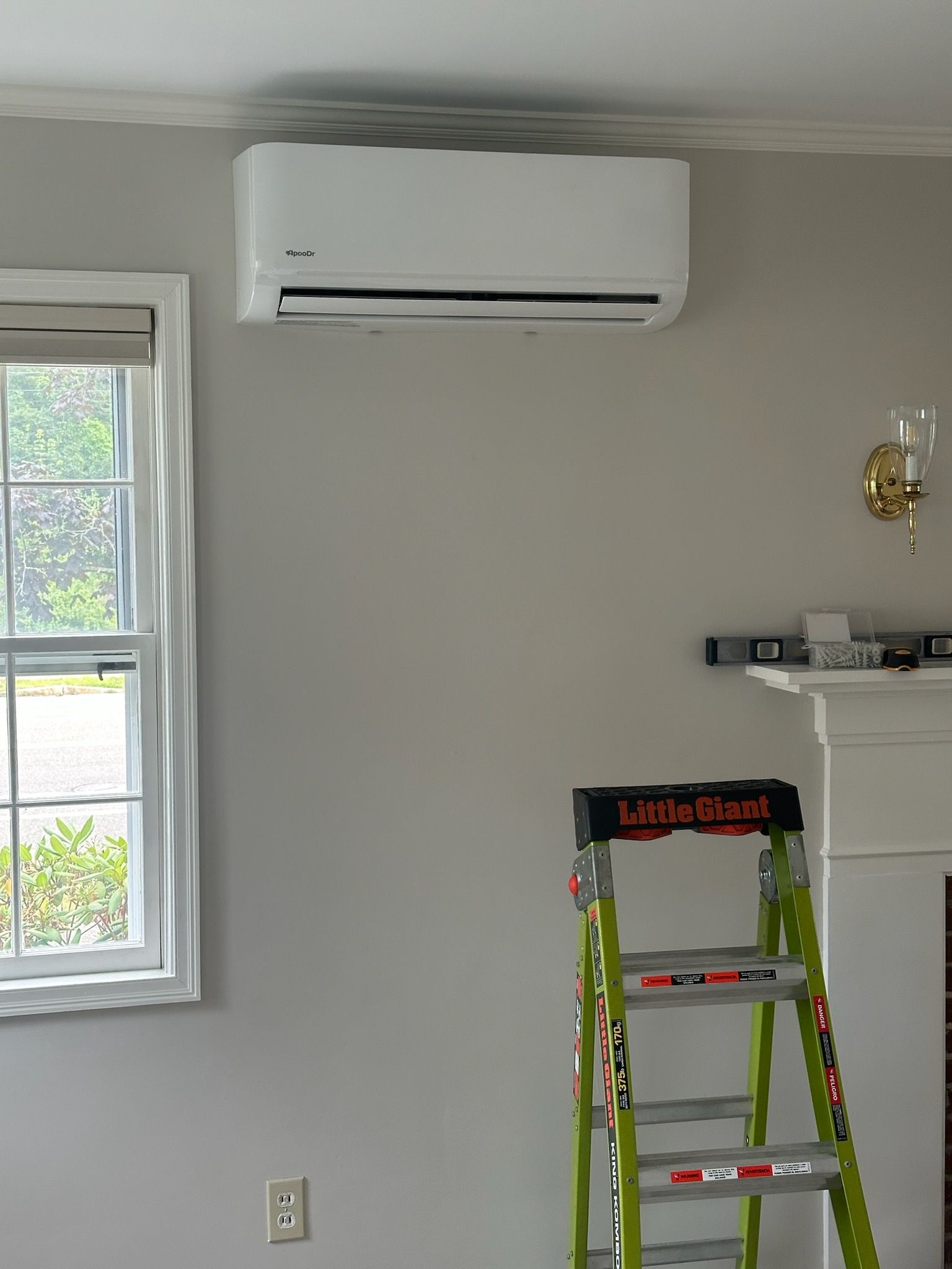 Wall-mounted air conditioner above a window in a room under renovation, with a ladder below.