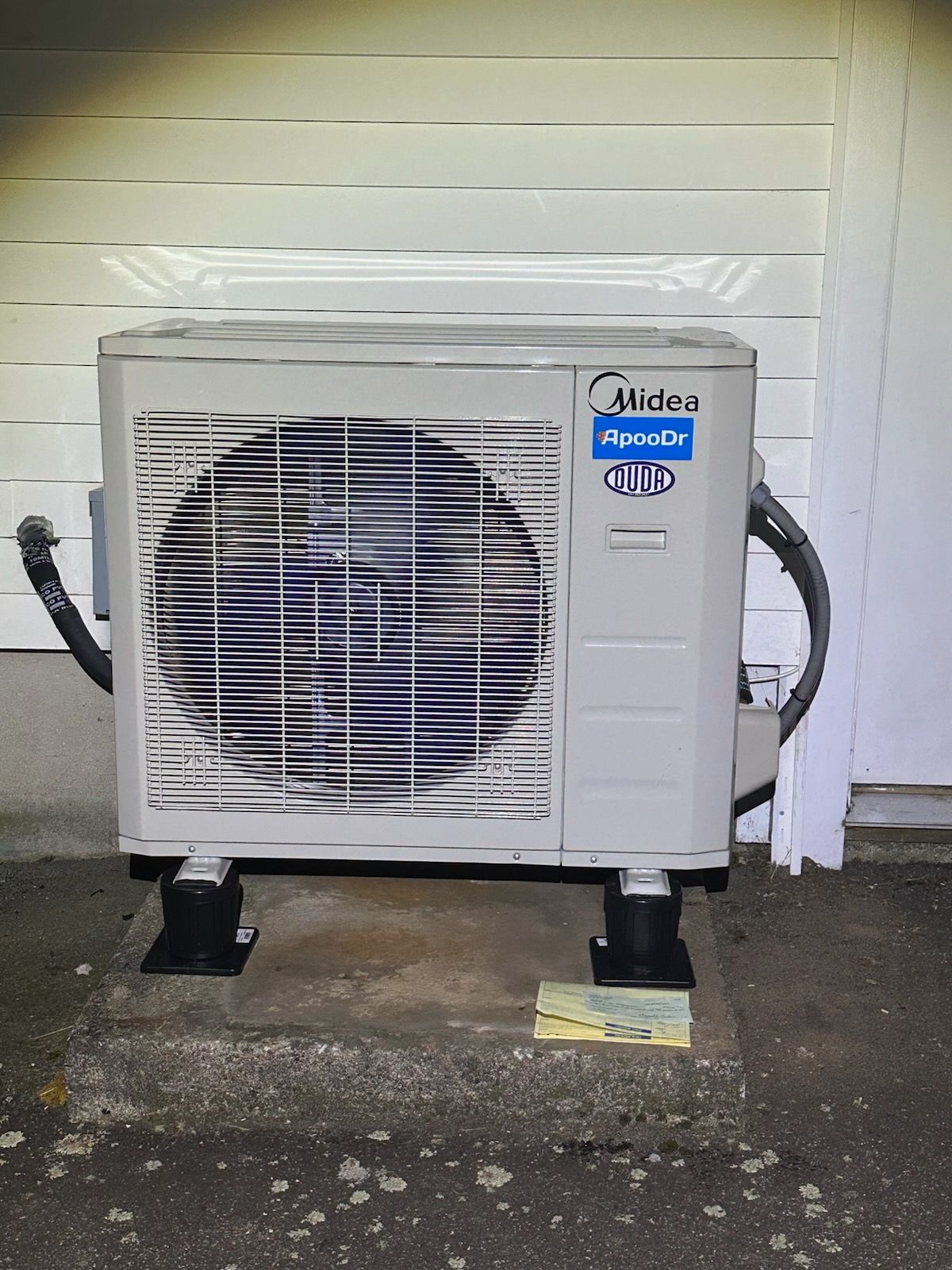 White outdoor air conditioner unit against a house wall with a fan behind a protective grille.
