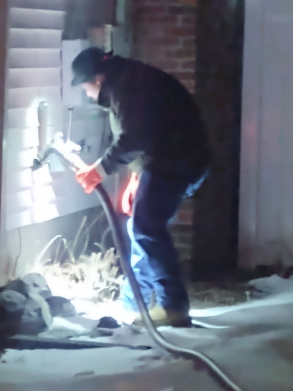 Worker using a power tool beside a wall at night, with extension cords on the ground.